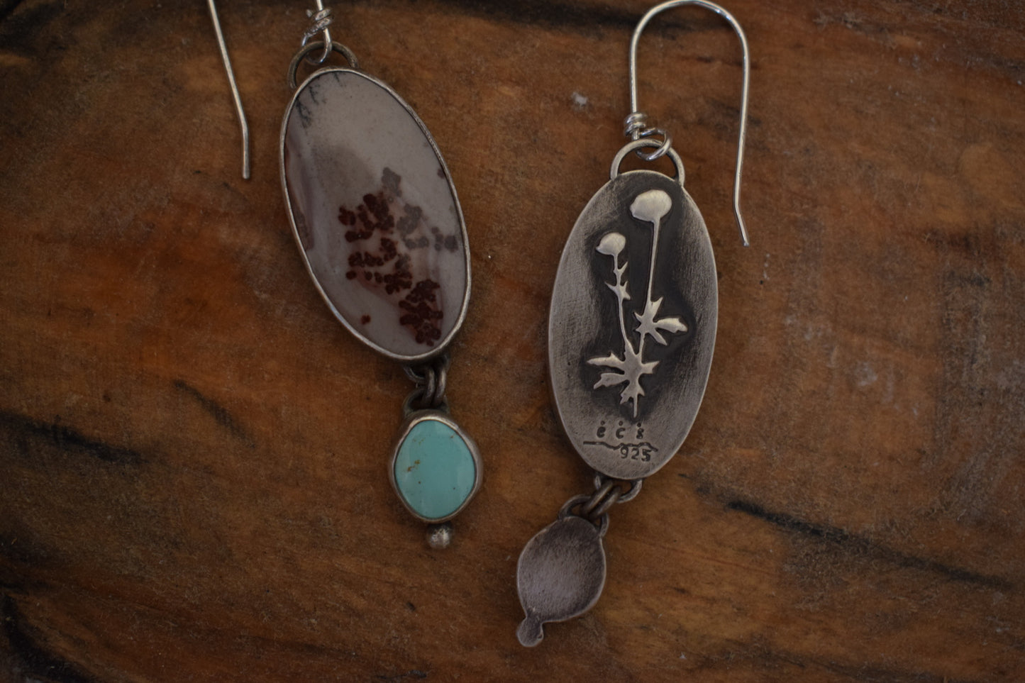 These earrings have two large maroon and grey stones with a marbled print, below them hangs light green turquoise dangles with small silver dot accents. The backside of the earrings has a small cutout of flowers and their leaves.
