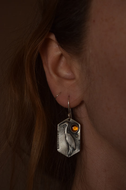 A silver crane sits on a six point backplate, with a dark baltic amber in the upper corner. Line stamped details fix the sides.