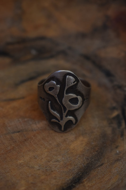 An elongated saddle ring has a hand cut poppy on the front.